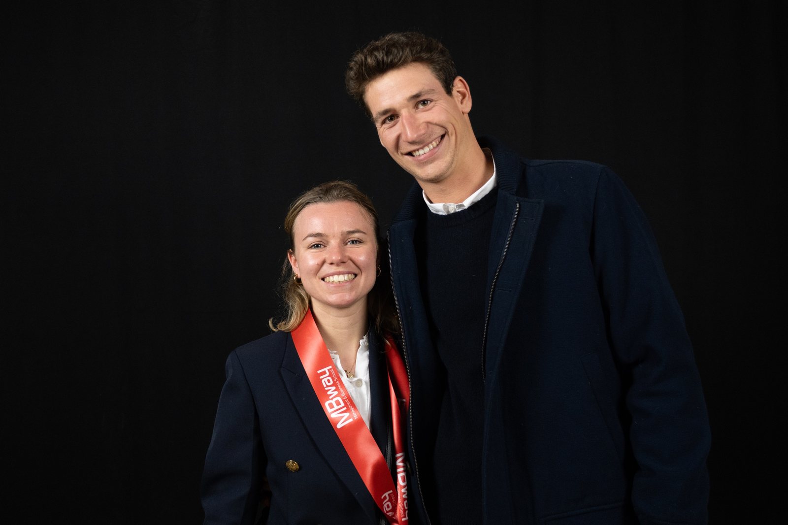 Deux diplômés posent devant le fond noir du photocall